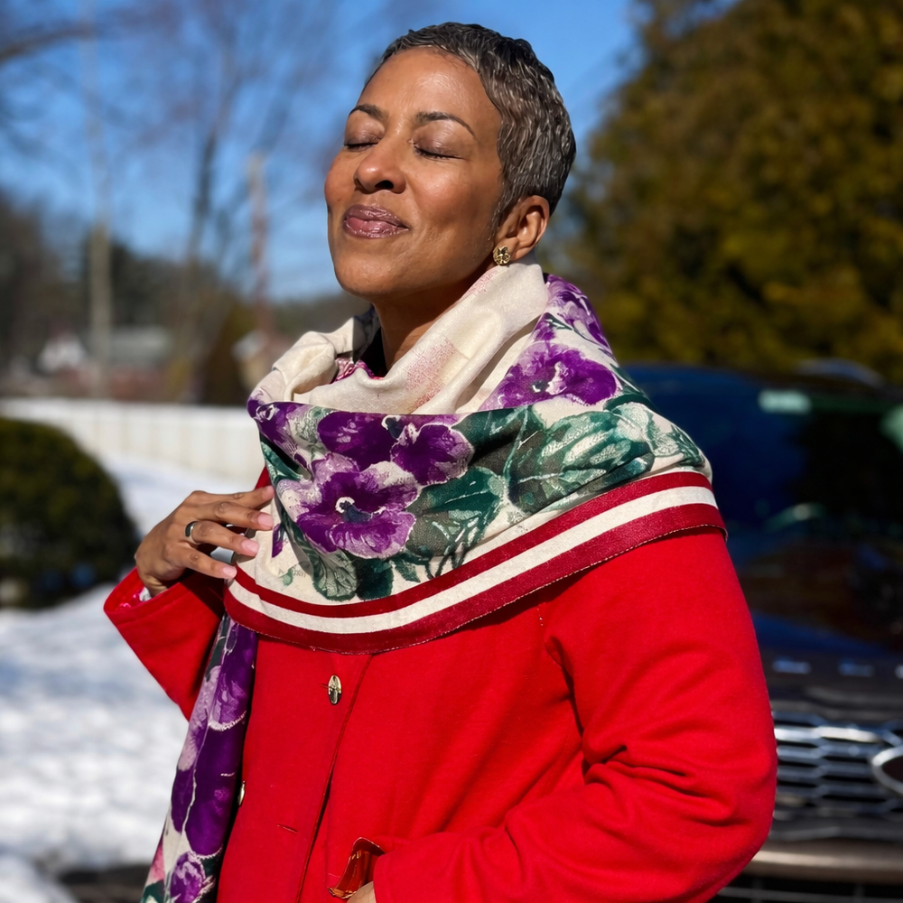 Woman wearing a red coat and purple violets scarf by Simply Greek outdoors with blurred background